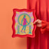 Colorful maximalist art print of a Greek godess on roller skates, set against a vibrant pink, orange, and green background with Greek columns.